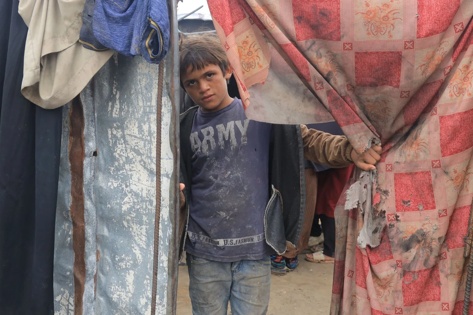 A boy standing at the entrance of a temporary shelter