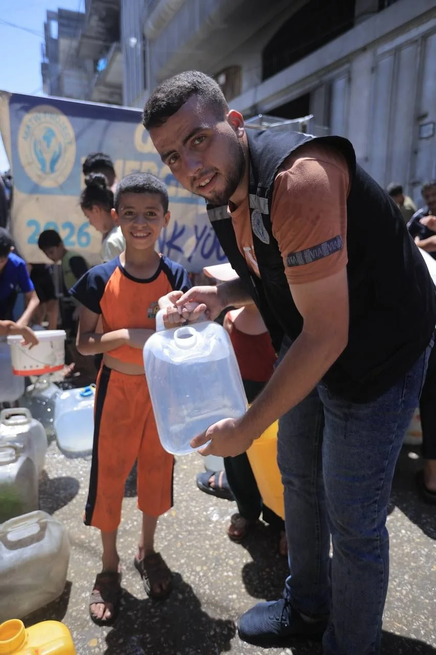 A child standing beside a man carrying a water container during a distribution